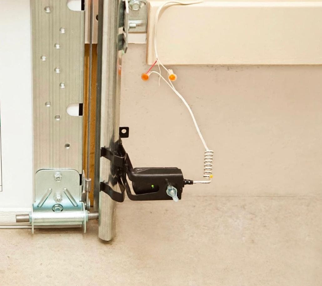 Garage door safety photo-eye sensor mounted at the base of the track with its indicator light lit