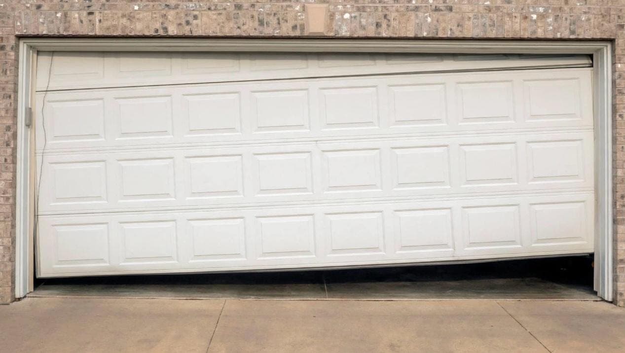 White garage door hanging off its tracks and sagging on one side on a Las Vegas brick home